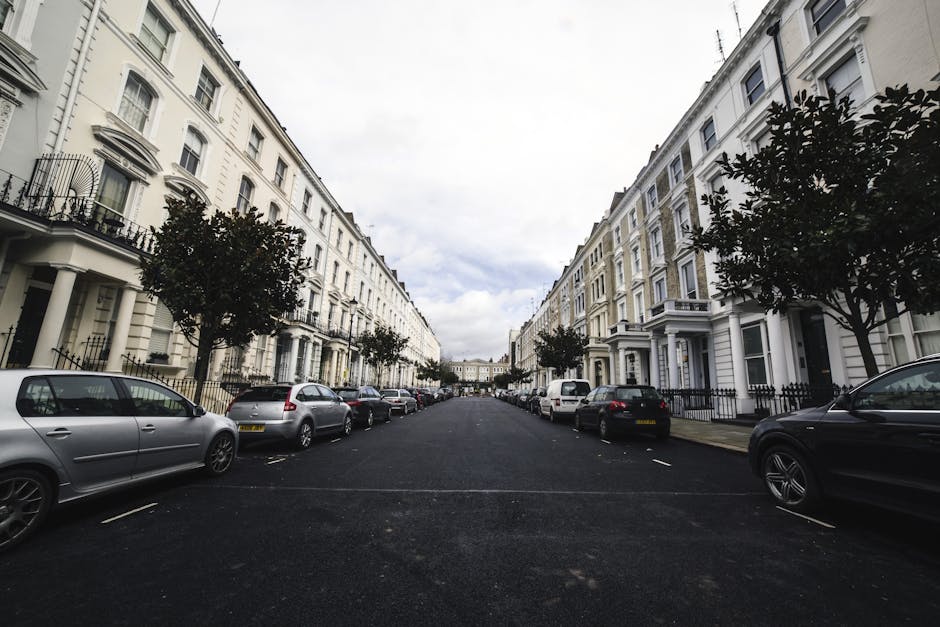 A wide residential street in Enfield with rows of white Victorian-style terraced houses featuring bay windows, decorative railings, and front steps, lined by parked cars on both sides including sedans